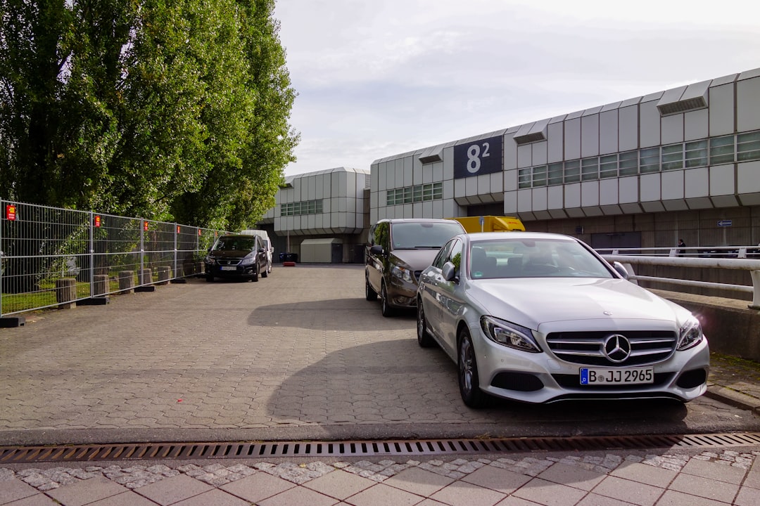 Silver mercedes-benz parked near a modern building with trees.