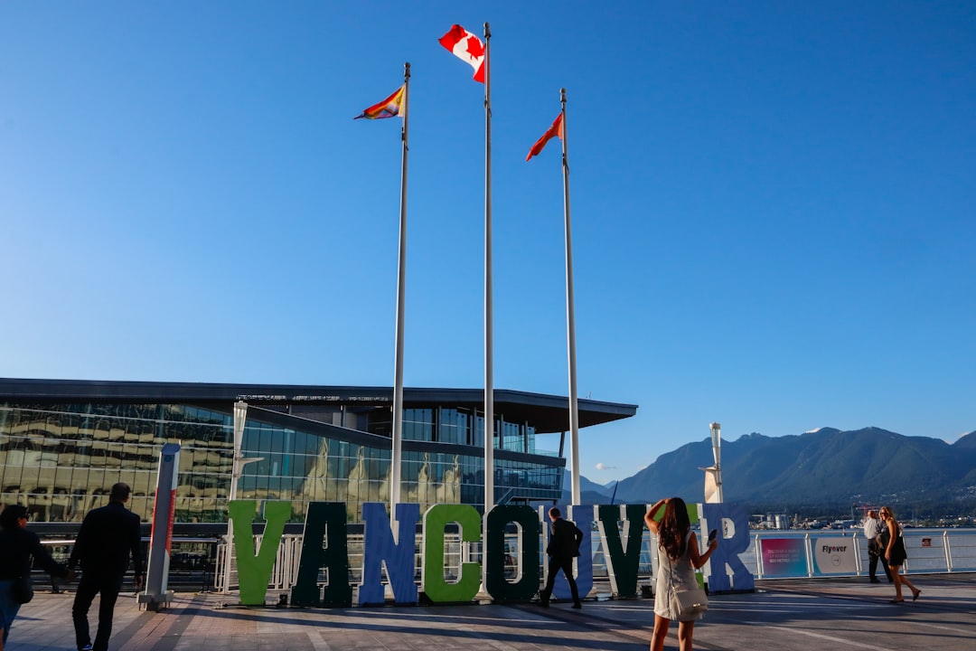 Vancouver sign, flags, and mountains against a clear blue sky.