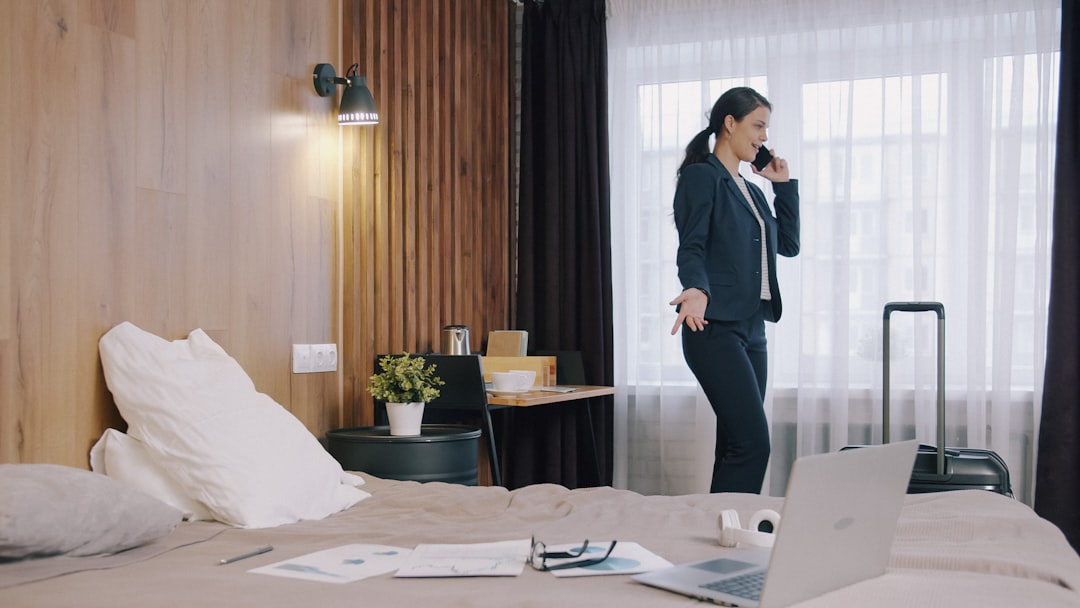 A woman in a dark suit talking on a phone in a hotel room