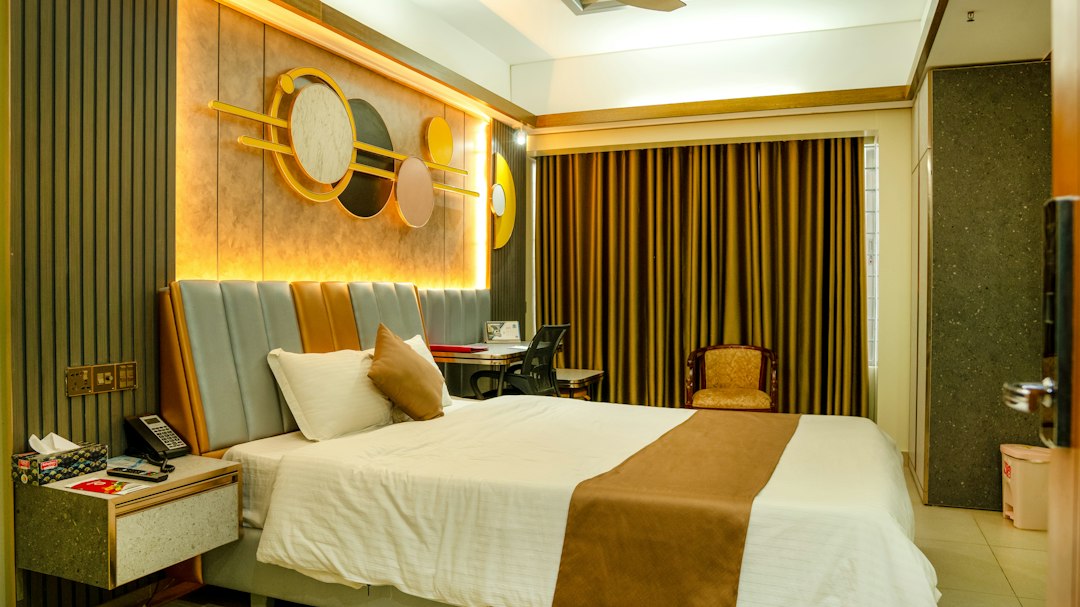 A hotel bedroom with a bed, desk, and gold wall art with backlighting